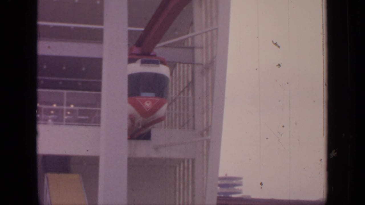 Red and white suspended cable car beside a multi-level structure.