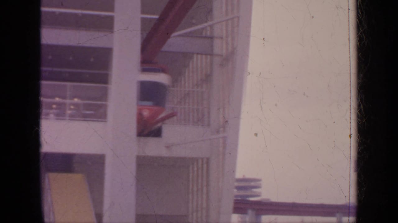 Suspended cable car partly hidden behind building columns.