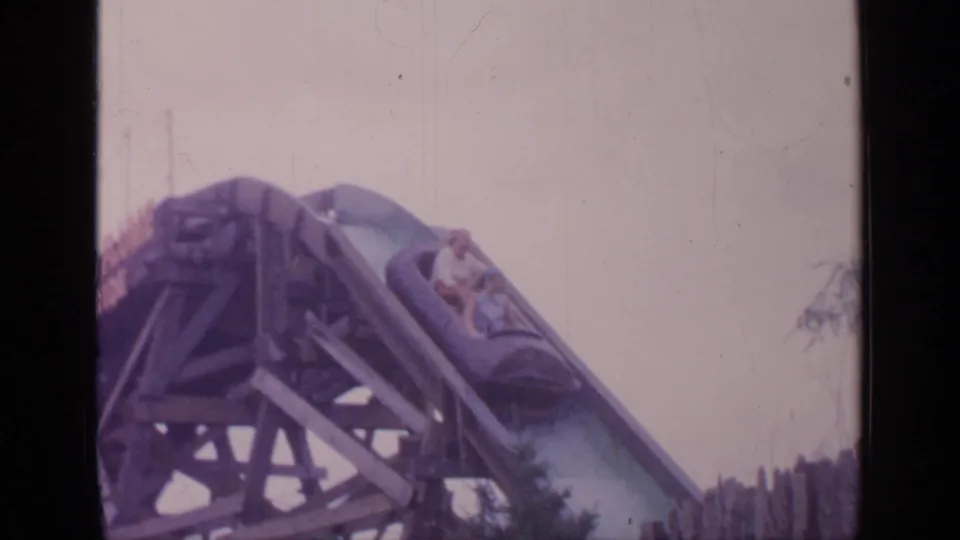 Riders in a roller coaster car enter the steep drop in faded 1964 Flushing Meadows 8mm footage.