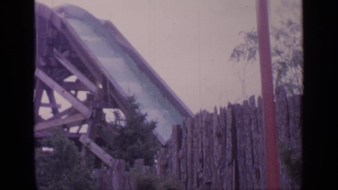 Log drop ride structures seen behind a wooden fence and trees.