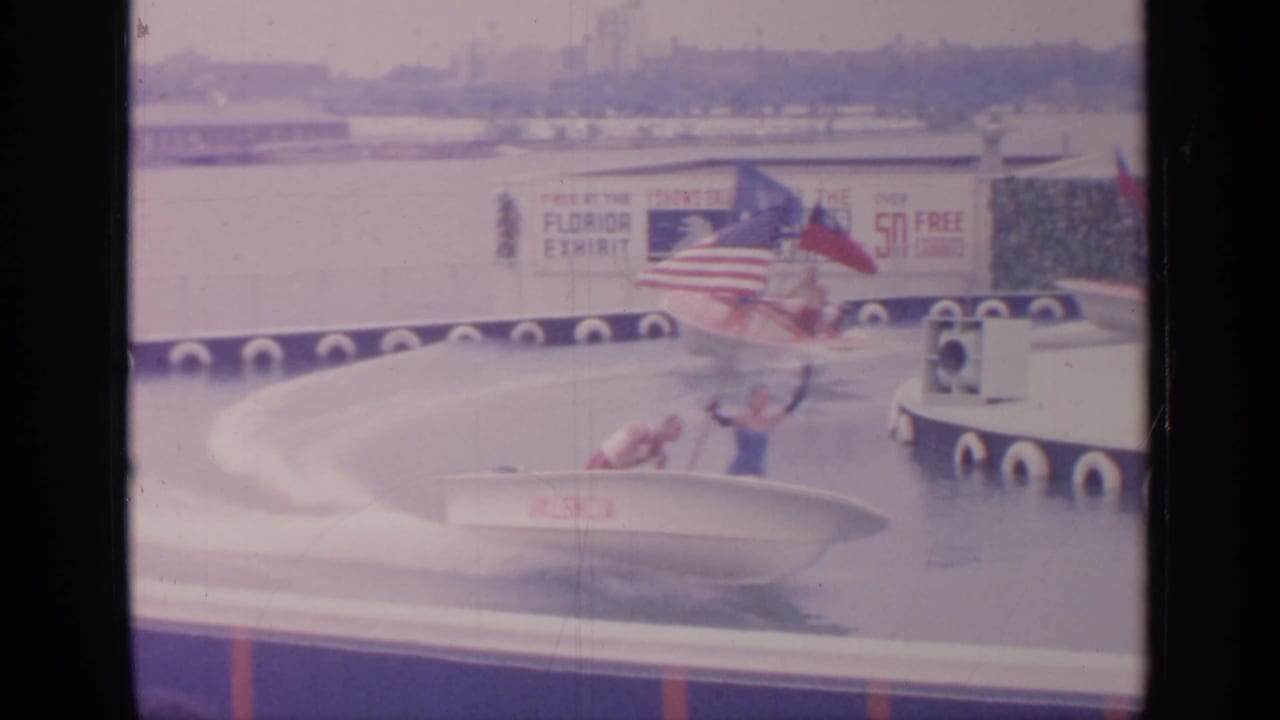 Two girls in small white boats on a circular water course with exhibit signs and flags behind them.