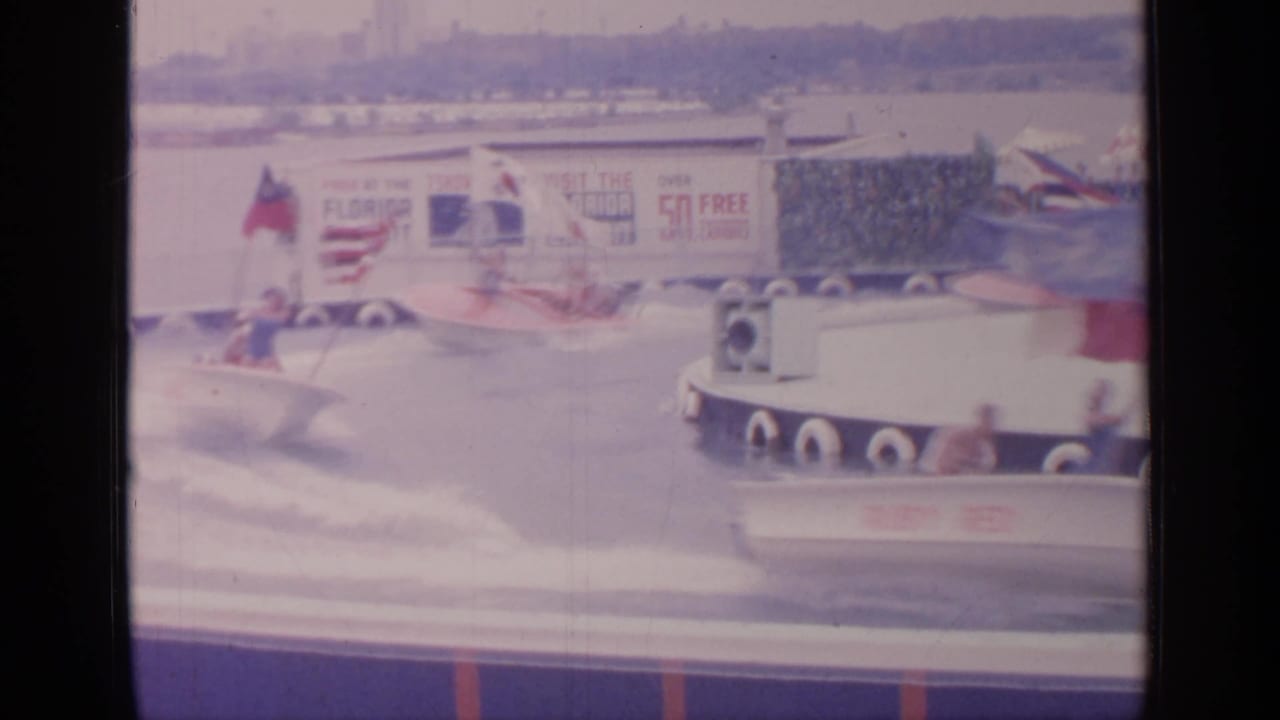 Small boats pass each other on the water course with flags and Florida exhibit signage in the background.