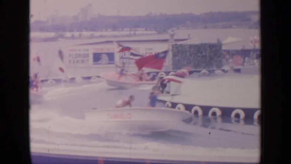 Home-movie frame from the 1964 fair showing a girl raising a flag from a white boat during the water attraction race.