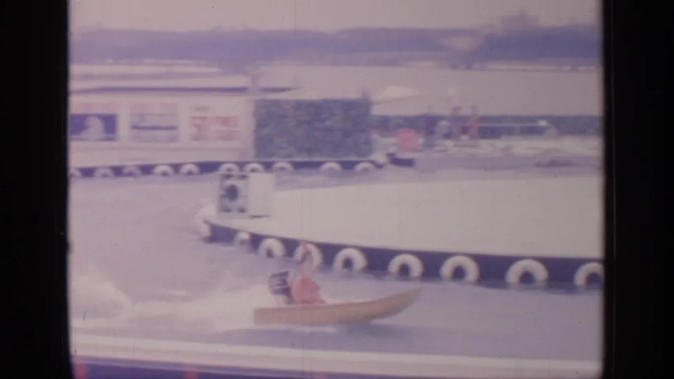 A speedboat with a visible rider turns near the foreground at the 1964 Flushing Meadows fair water course, with exhibit signage behind.