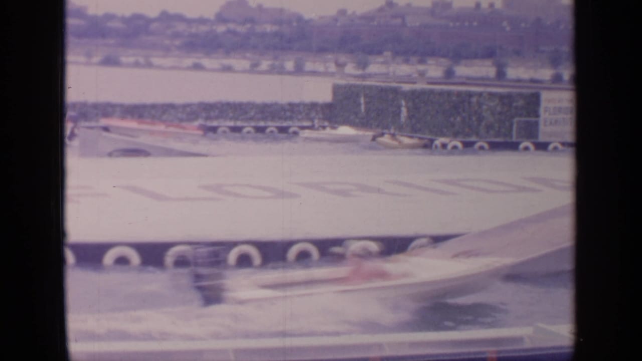 Water performer speeds past a ramp with spray in front of exhibition signage and a ship-like display.