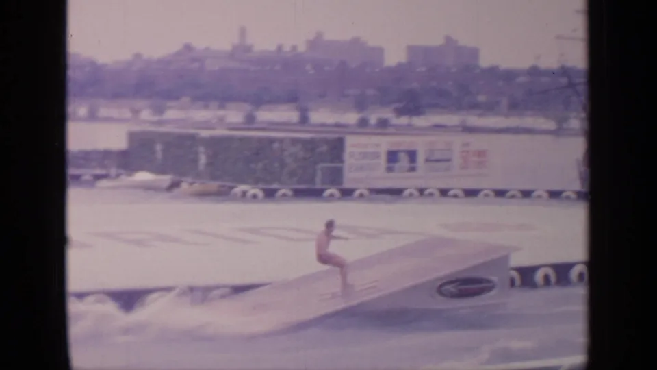 At the 1964 Flushing Meadows World's Fair, a water performer appears on the ramp above the pool, with signage and fair structures behind him.