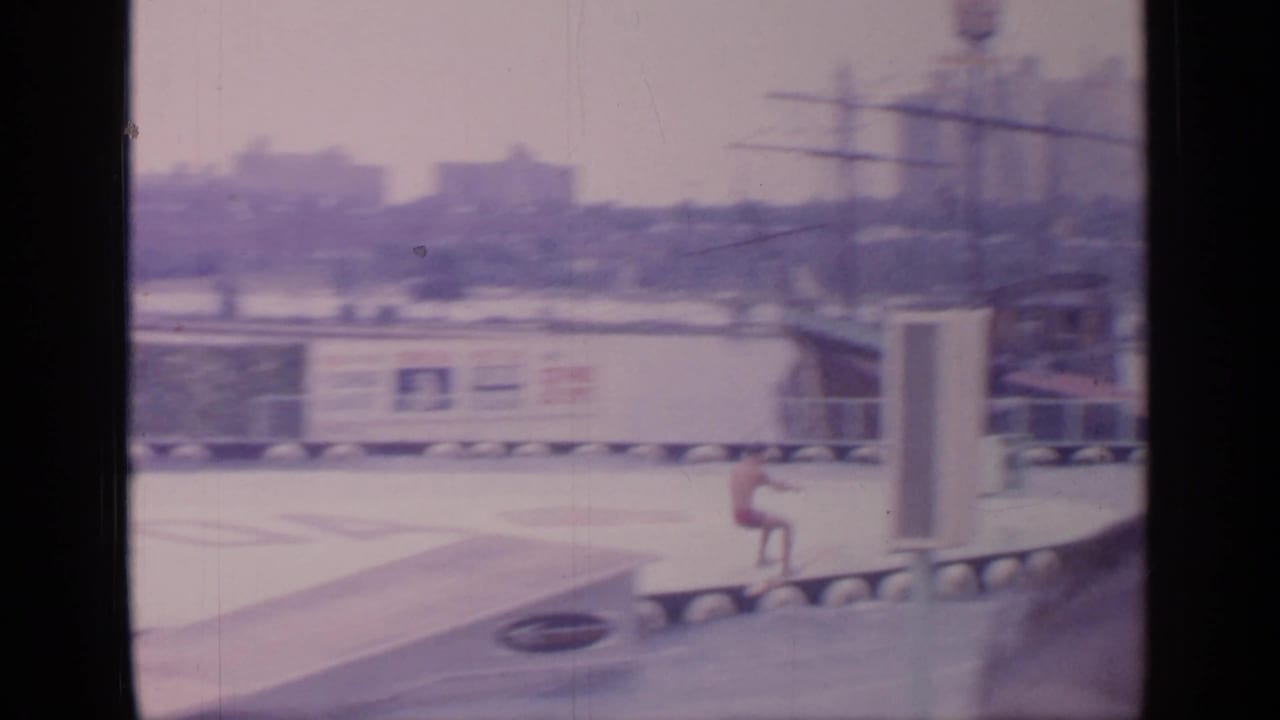 Outdoor fairground pool with a water-ski performer near a ramp and exhibit structures in the distance.