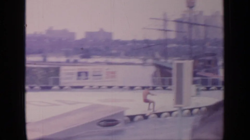 1964 Flushing Meadows fair attraction scene with a water-ski performer near a ramp and Florida Exhibit area structures visible through soft 8mm framing.