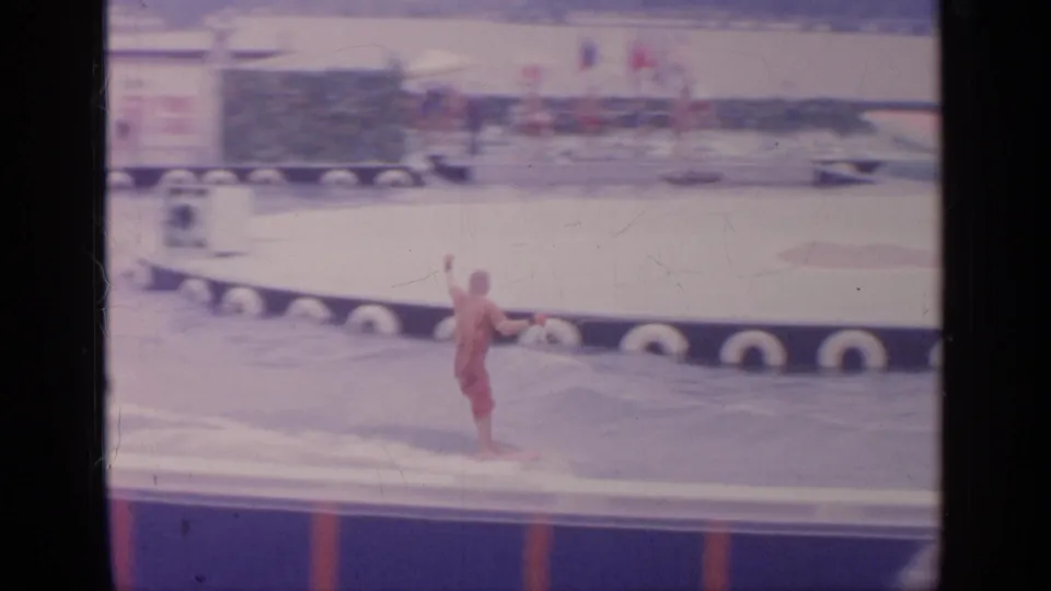 A red-clad water-ski performer passes near the edge of the Florida Exhibit pool at the 1964 World's Fair, seen in faded 8mm color.