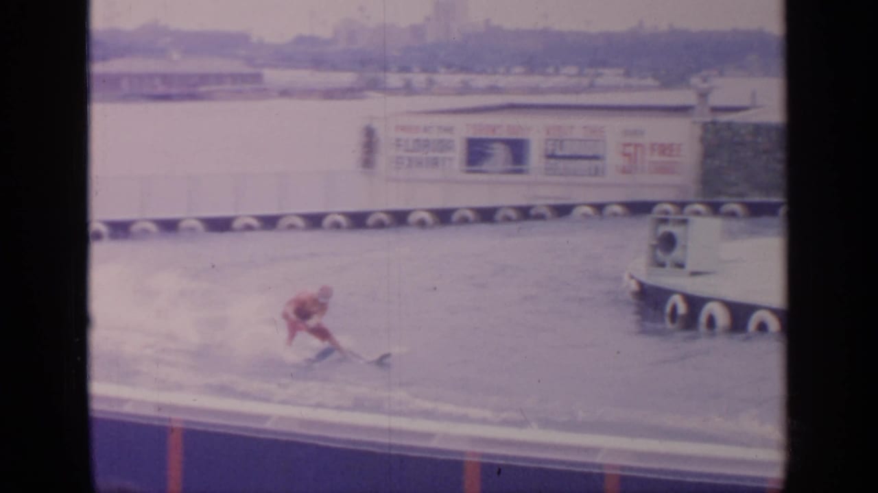 Water skier leaning into the spray near a tow boat and exhibition sign.