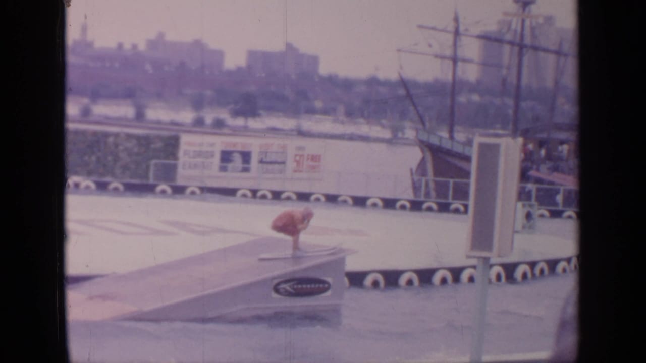 A water skier in red launches from a ramp beside floating platforms and exhibit signage.