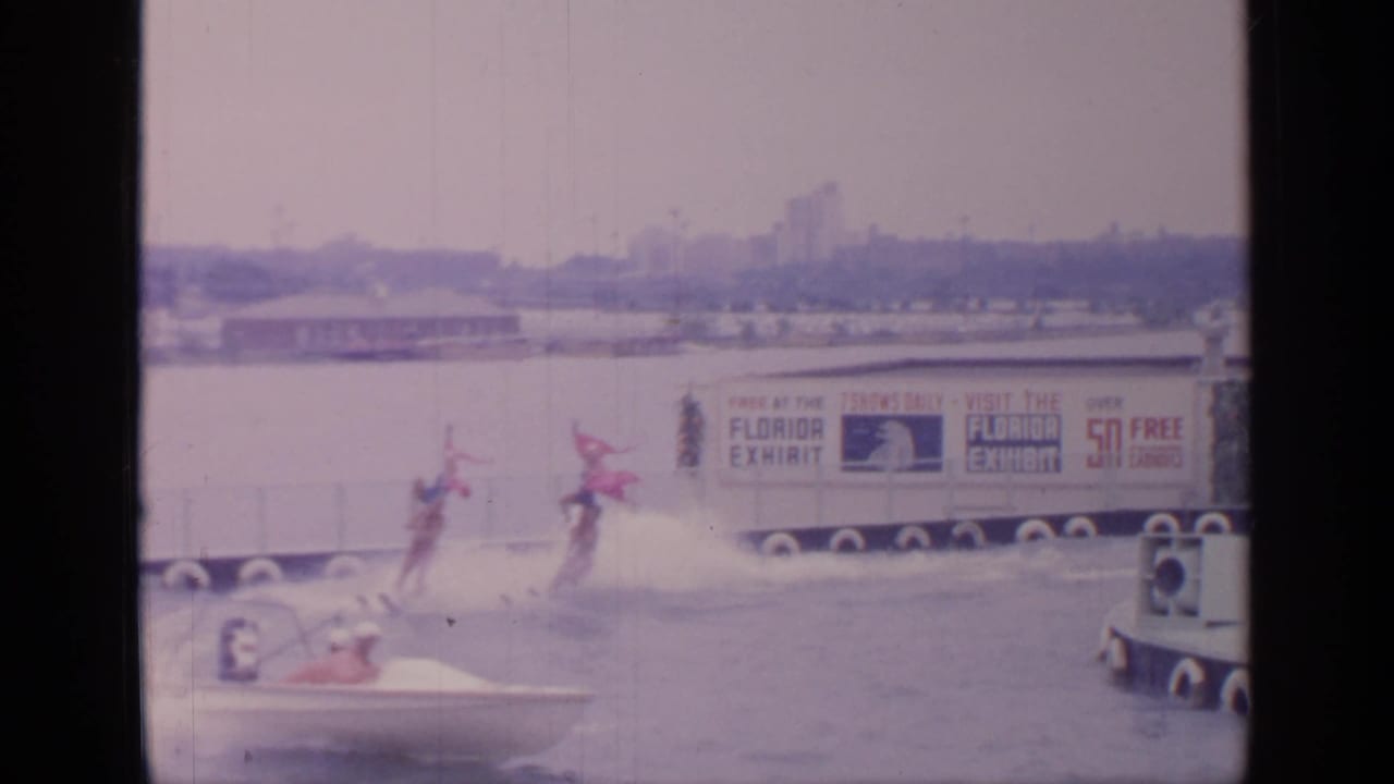 Two skiers move across the water near a small boat and Florida exhibit banner in the 1964 Flushing Meadows fair footage.