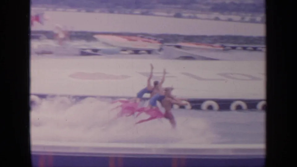 Synchronized waterskiers in bright costumes lean across the water in a visitor-shot 1964 Flushing Meadows fair scene.