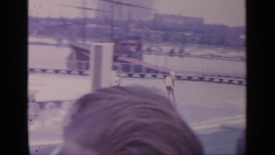 1964 Flushing Meadows home-movie frame showing a water skier on a circular pool, partly blocked by nearby spectators.
