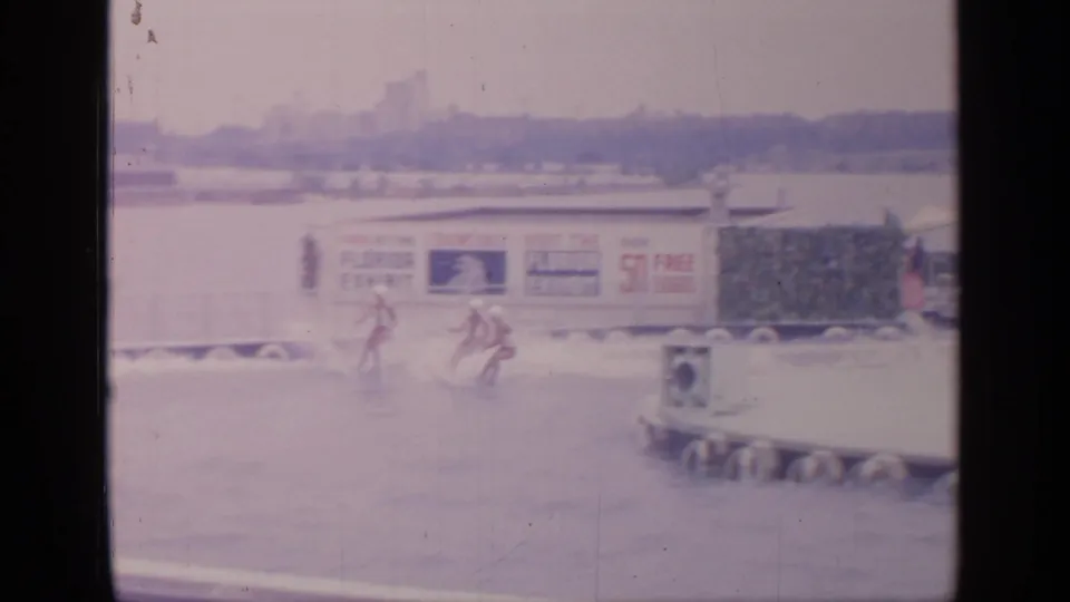 1964 Flushing Meadows frame with two water skiers near Florida exhibit signage and a circular pool edge.