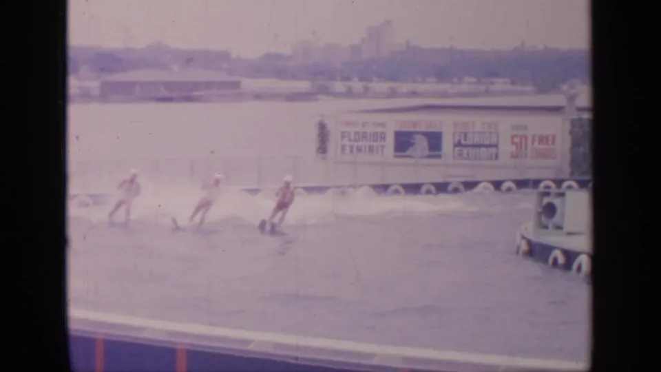 At Flushing Meadows in 1964, water skiers move across the lake with Florida Exhibit signage and fair structures in the background.