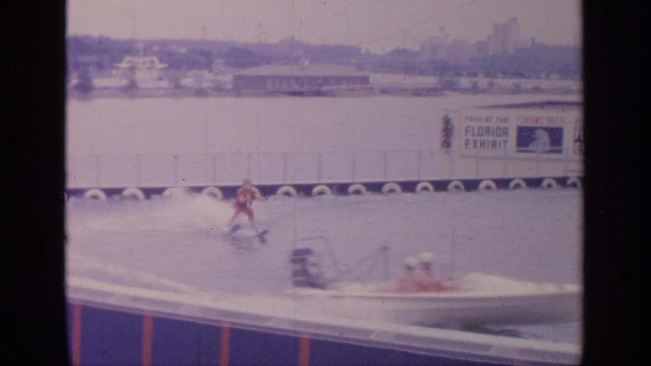 Waterskier in red swimwear moves across water near a tow boat and Florida Exhibit signage.