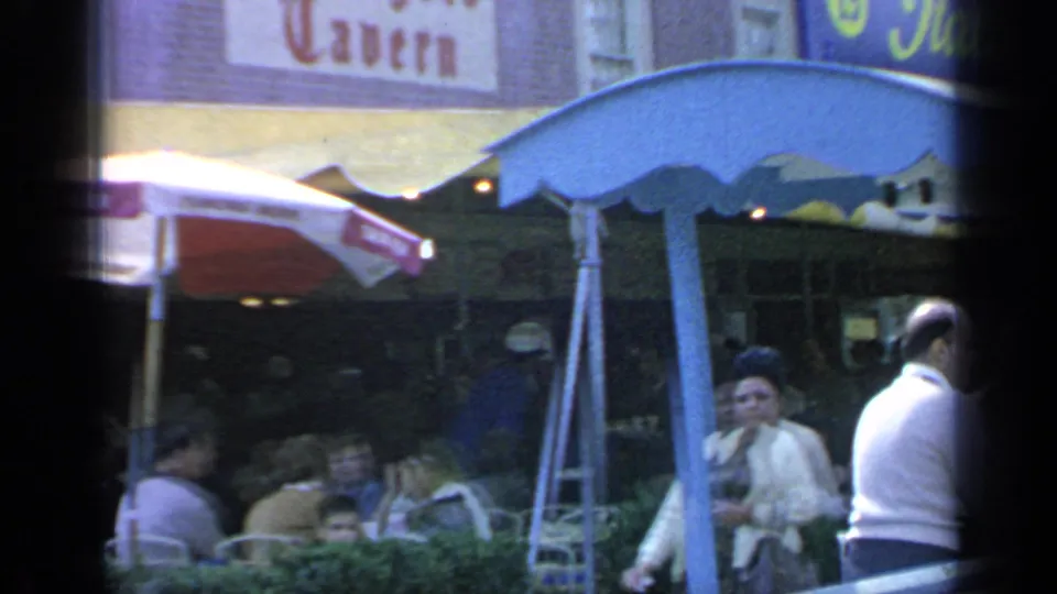 Visitors gather beneath the Rheingold Tavern sign at Flushing Meadows, with patio umbrellas and shaded seating visible.