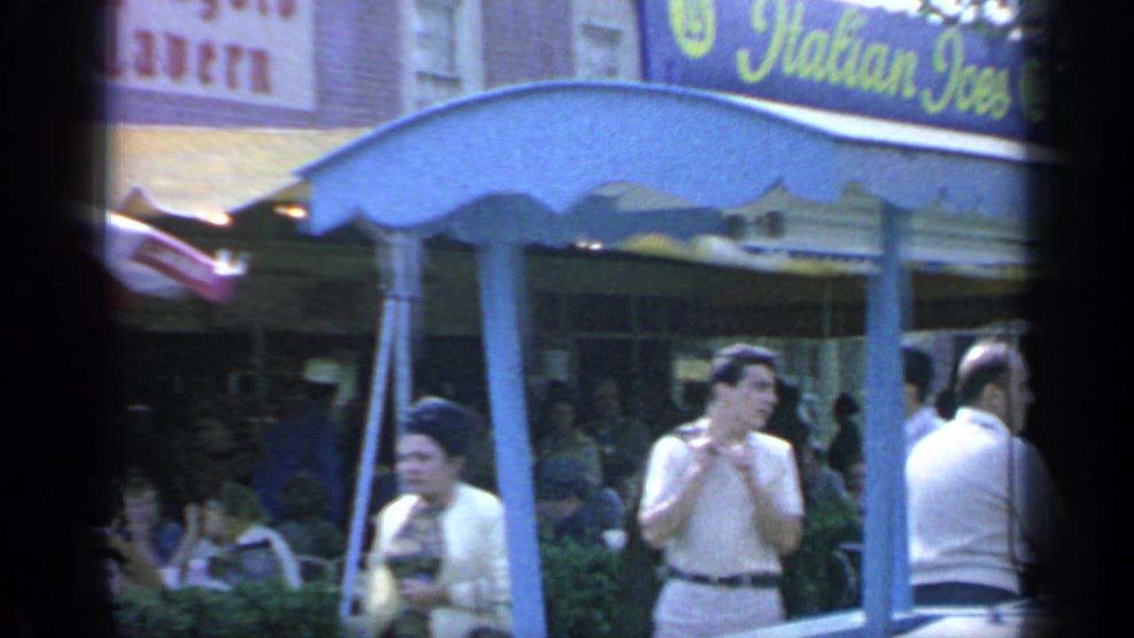 Visitors stand near a blue-canopied food stand with Italian ice signage.