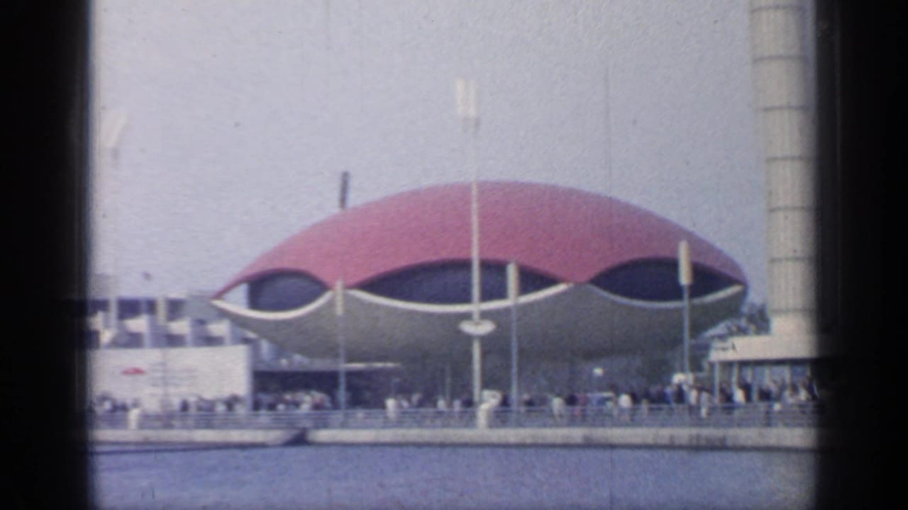 Red-domed fair building beside water with crowds on a promenade.