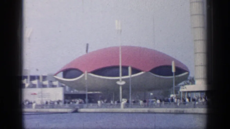 1964 Flushing Meadows World's Fair view of a red-domed pavilion, waterfront, light poles, and small crowds along the promenade.
