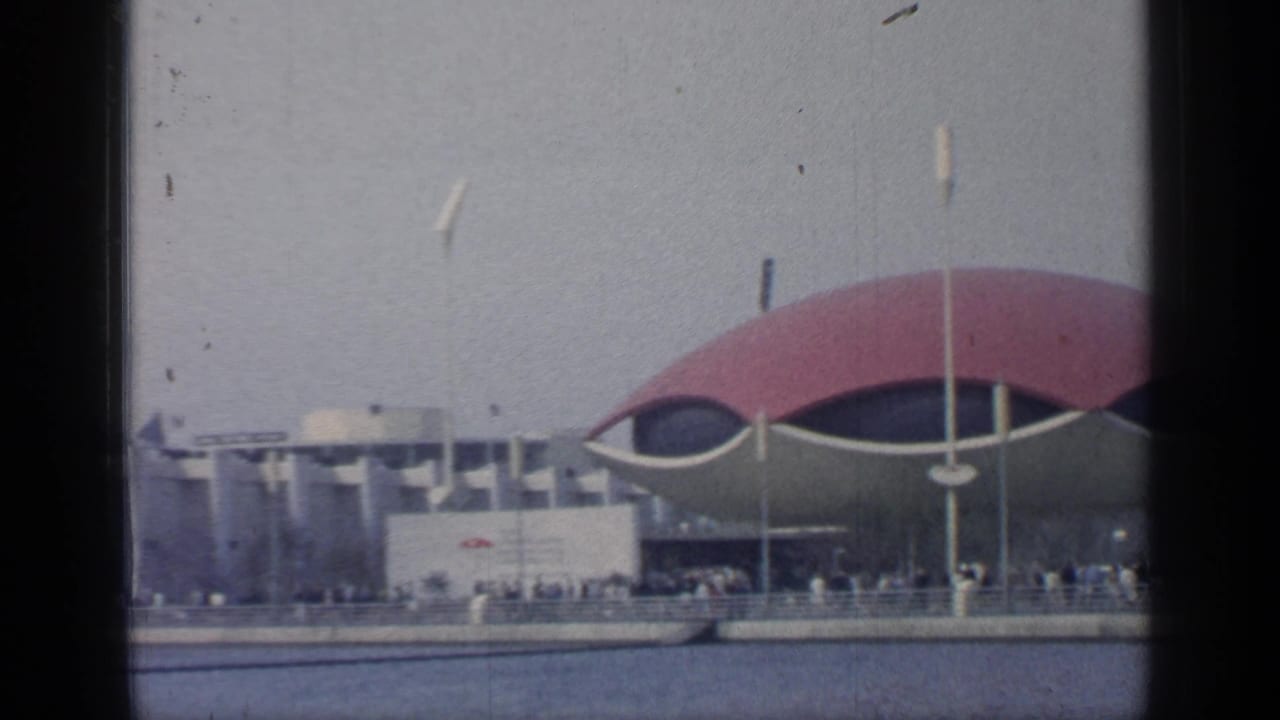 Fairground pavilion and waterfront promenade seen through dark film edges.