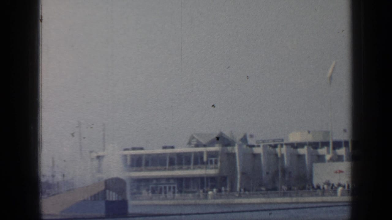 Distant modernist fair pavilion seen across water with dark film borders.