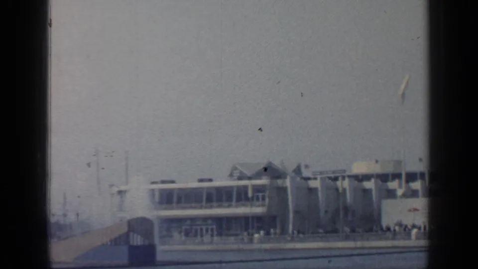 1964 Flushing Meadows World's Fair pavilion viewed from a moving boat across water under a hazy sky.