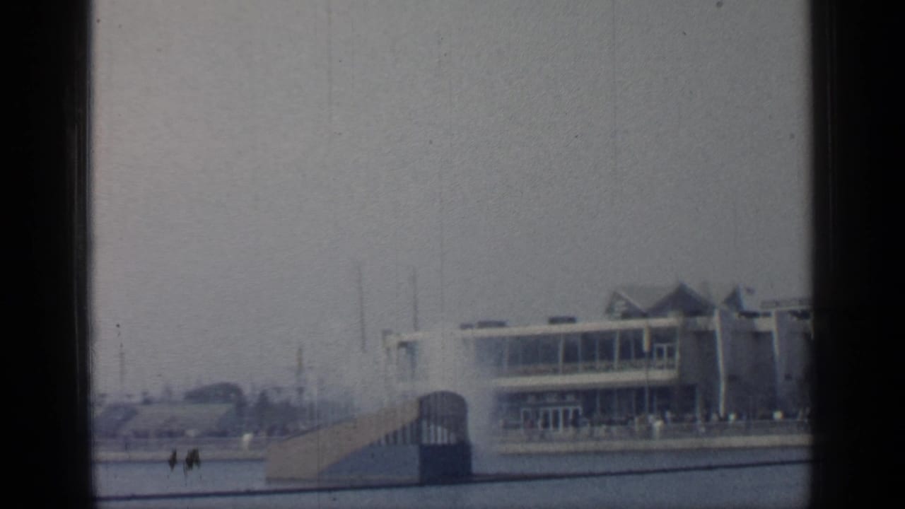 Fair building and ramp seen from water with small distant people nearby.