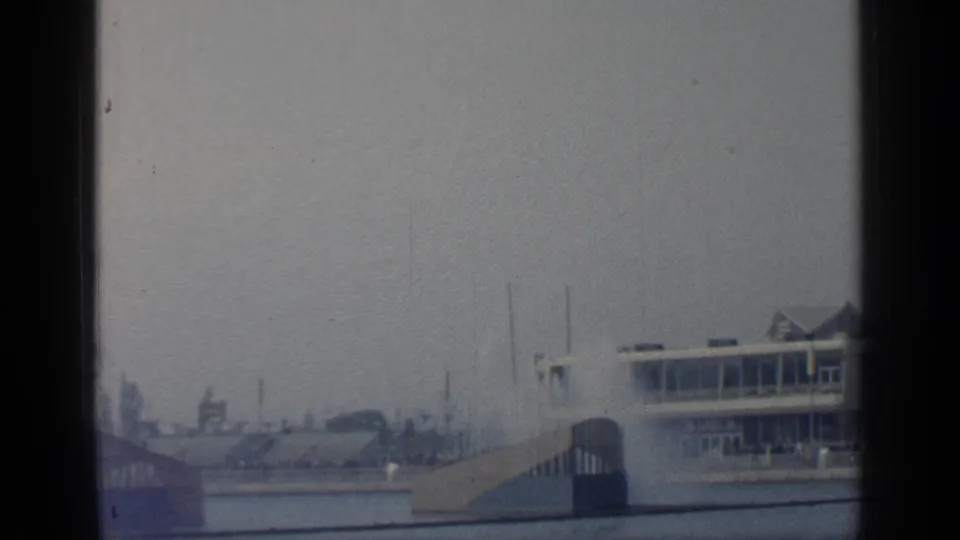 A soft 8mm view of the World's Fair grounds shows part of a pavilion, ramp, water, and distant structures.