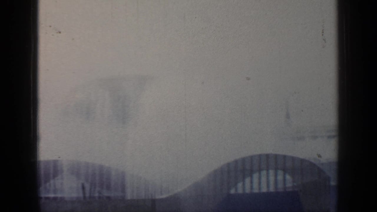 Hazy fairground view with arched structures, mist, and dark window-like borders.