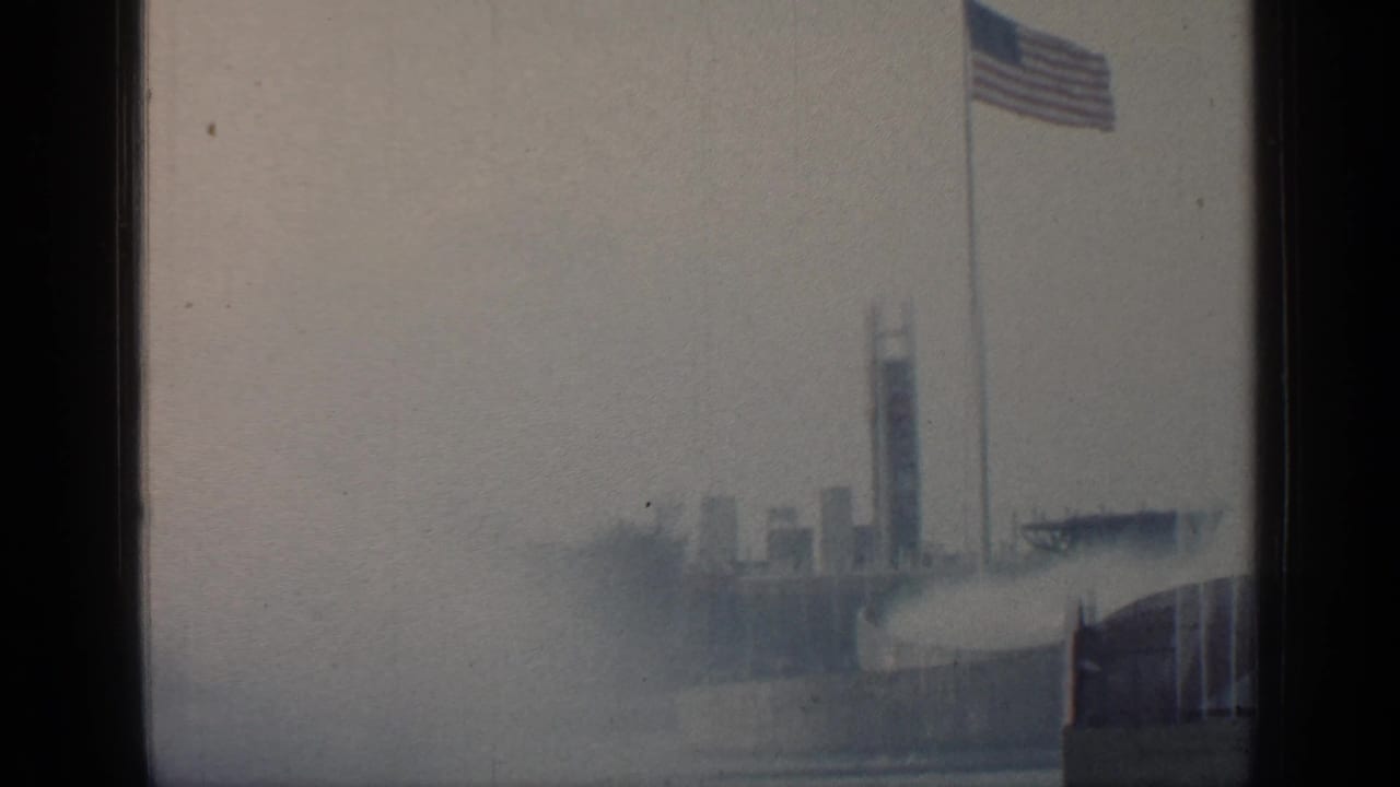 American flag above distant fair structures in soft-focus 8mm footage.