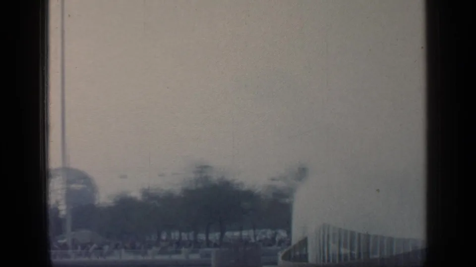 1964 Flushing Meadows frame showing trees, fencing, and partial fair architecture in soft, grainy home-movie exposure.