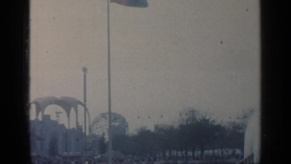 Distant 1964 Flushing Meadows view with the Unisphere visible near fair structures and trees under an overcast sky.