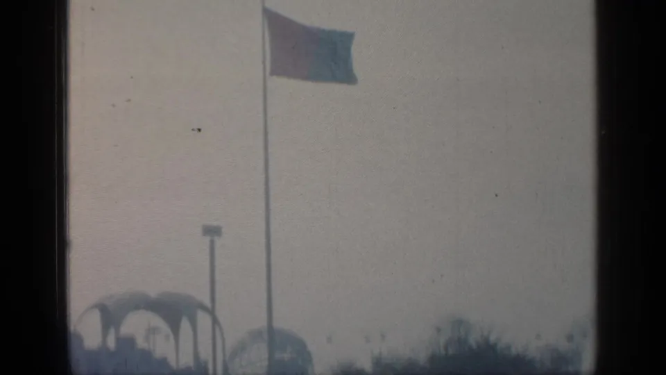 Visitor-shot 1964 Flushing Meadows World's Fair view with a flagpole, arched structures, and hazy distant fair architecture.