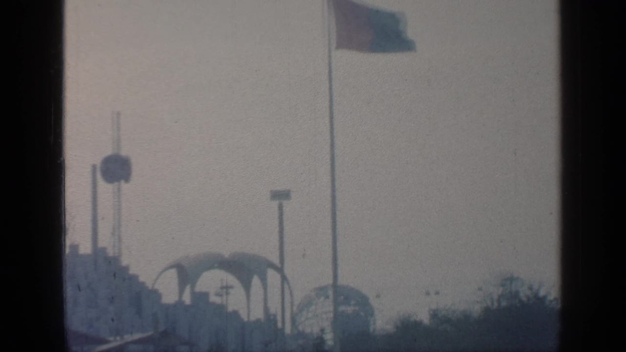Fairground skyline with poles, a round feature, arches, and a flag at right.