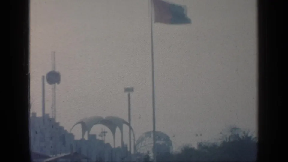 1964 Flushing Meadows World's Fair structures appear through haze, with vertical poles, a round architectural feature, arches, and a flag.