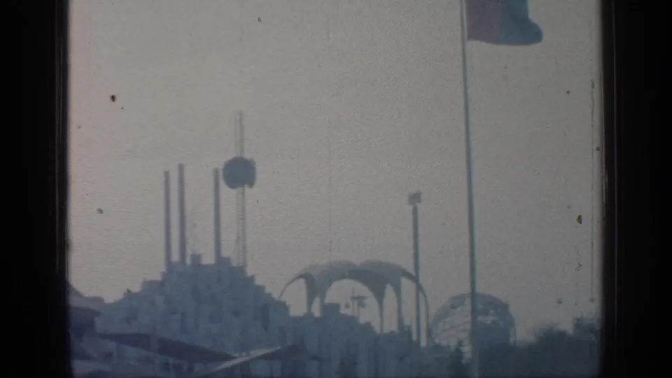 Distant 1964 World's Fair scene at Flushing Meadows with tall vertical elements, a round feature, arched forms, and a flagpole.