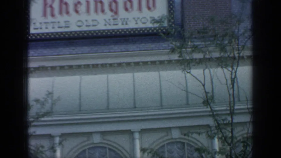 1964 Flushing Meadows fair scene showing a partial Rheingold sign, pale facade, arched windows, and foreground trees.