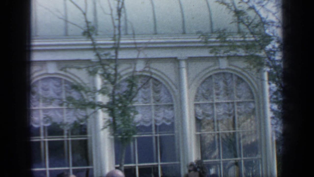 1964 Flushing Meadows view of tall arched windows, white columns, lace-like curtains, and trees from a handheld 8mm frame.