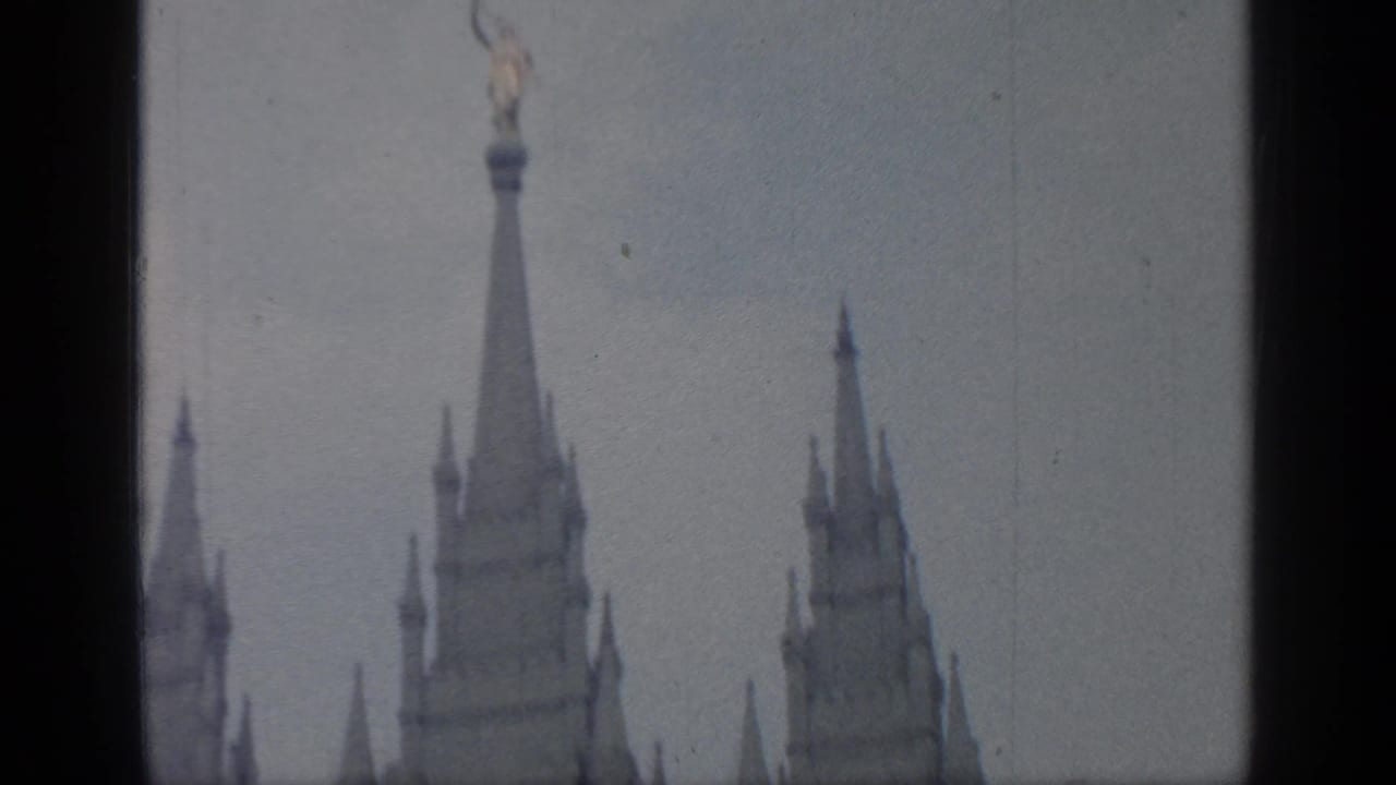 Tall pointed fair structures under a gray sky, framed by dark film edges.