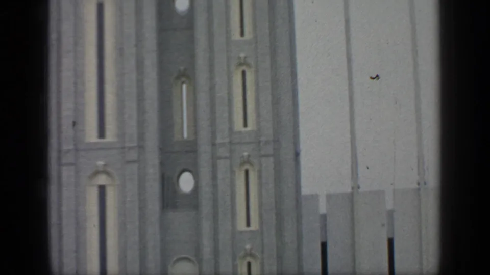 1964 Flushing Meadows home-movie frame of tall fair towers with narrow openings, soft grain, and dark film border.