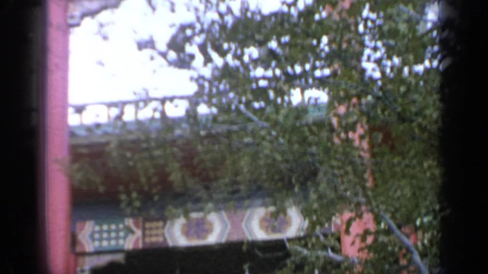 1964 Flushing Meadows fair structure with red columns and decorative trim seen through tree branches on 8mm film.
