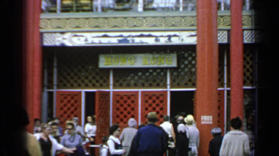 Visitors at the 1964 Flushing Meadows World's Fair gather beneath red columns near a visible Hong Kong sign.
