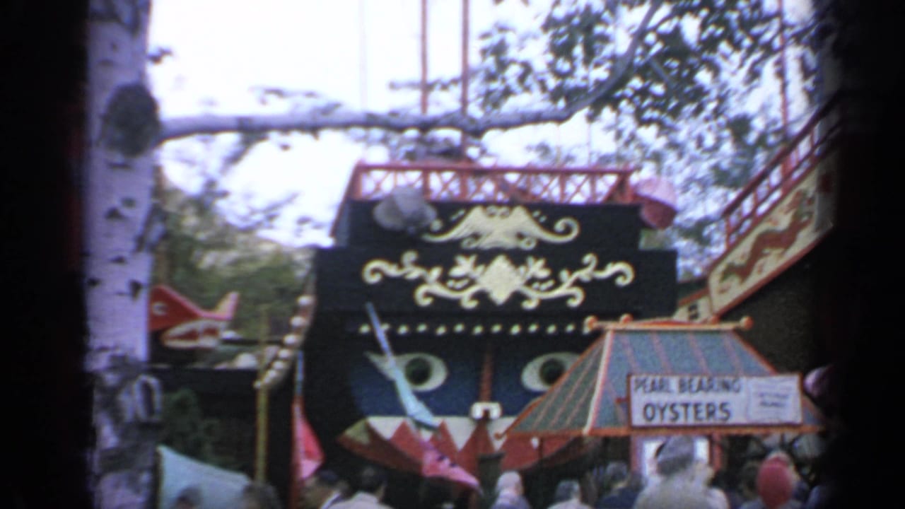 Crowd gathered near a Pearl Bearing Oysters sign and ornate boat-shaped fair attraction.