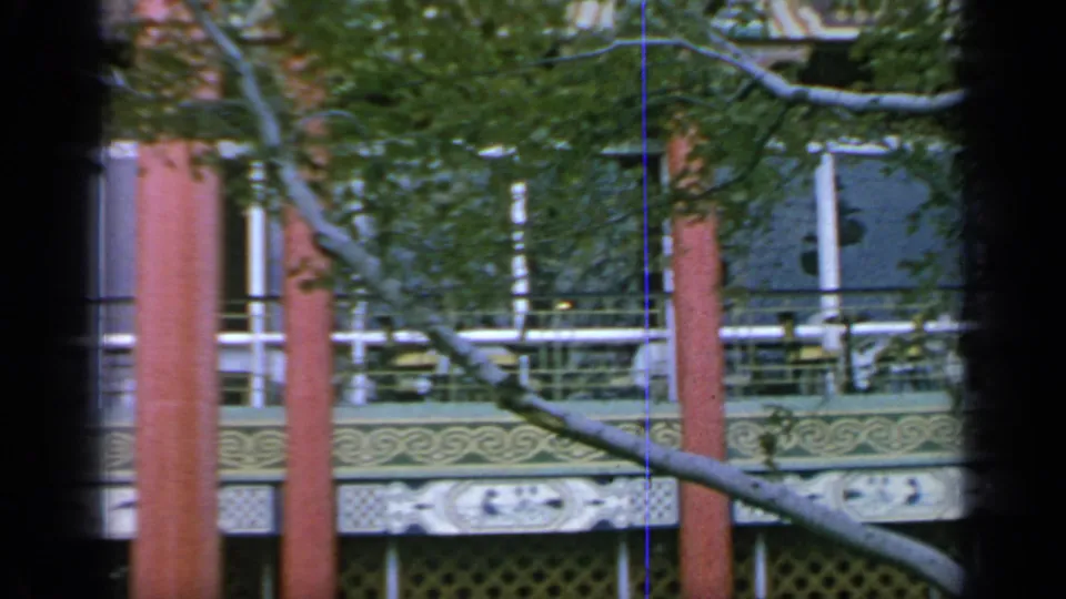 The camera pan shows the pavilion exterior at Flushing Meadows, with red columns, white railings, and leafy branches in front.