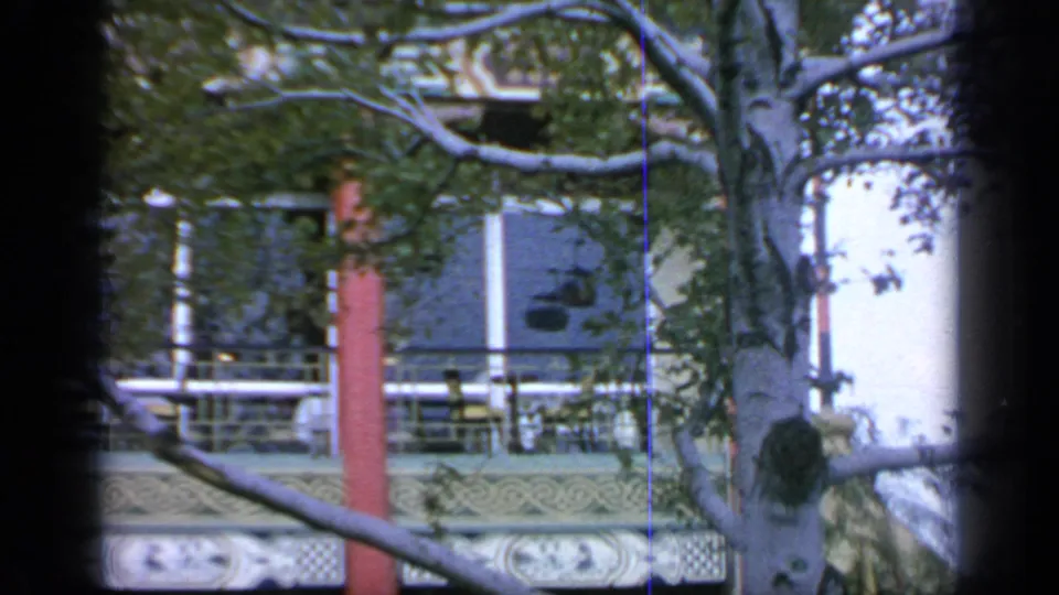 A visitor-shot 1964 frame shows the Hong Kong Pavilion balcony and windows partly hidden by a tree trunk and branches.