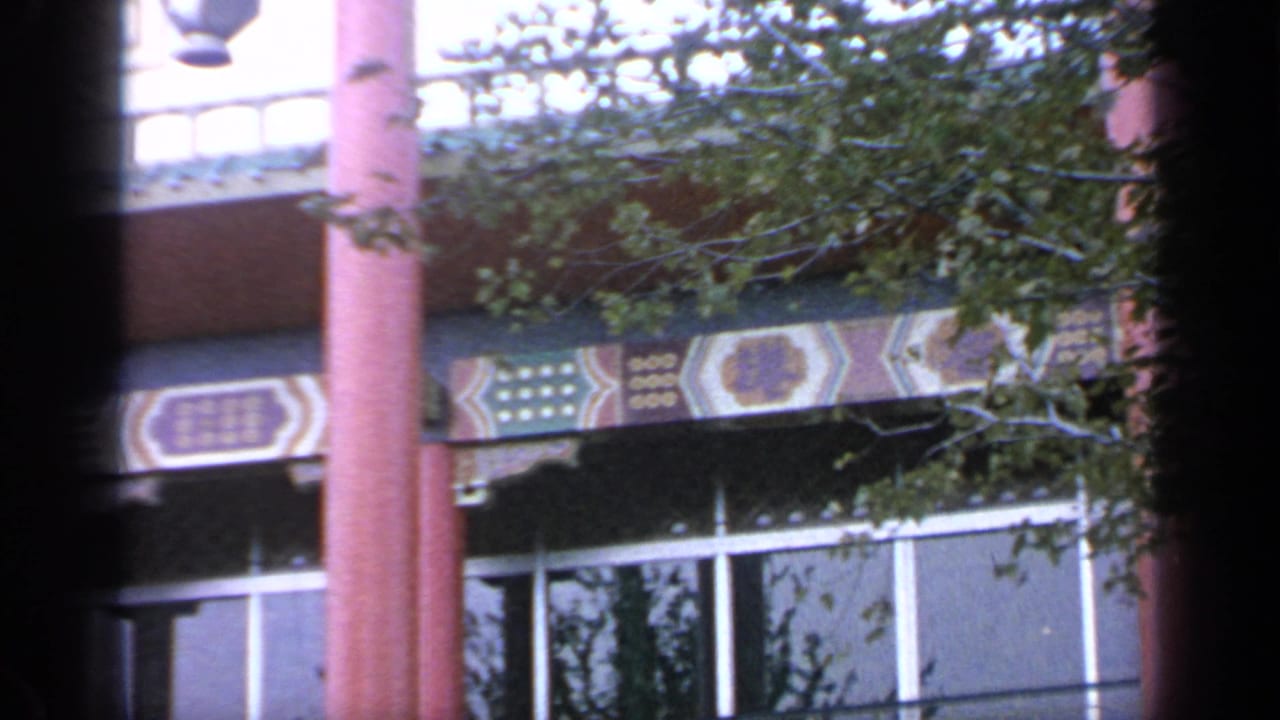 Flushing Meadows World's Fair building detail with red columns, geometric eaves, tree cover, and soft 8mm color.