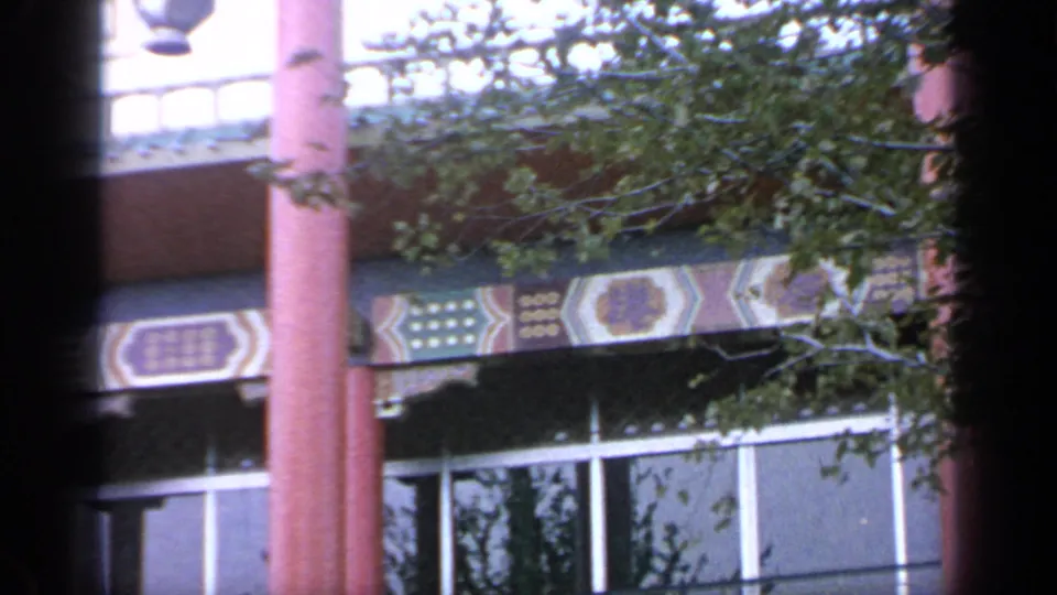 Flushing Meadows World's Fair building detail with red columns, geometric eaves, tree cover, and soft 8mm color.