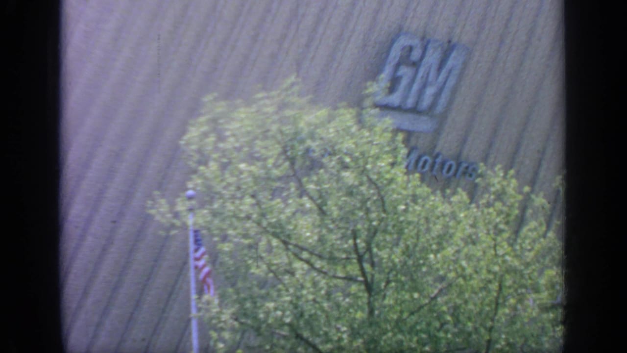 General Motors sign partly visible above trees and an American flag.